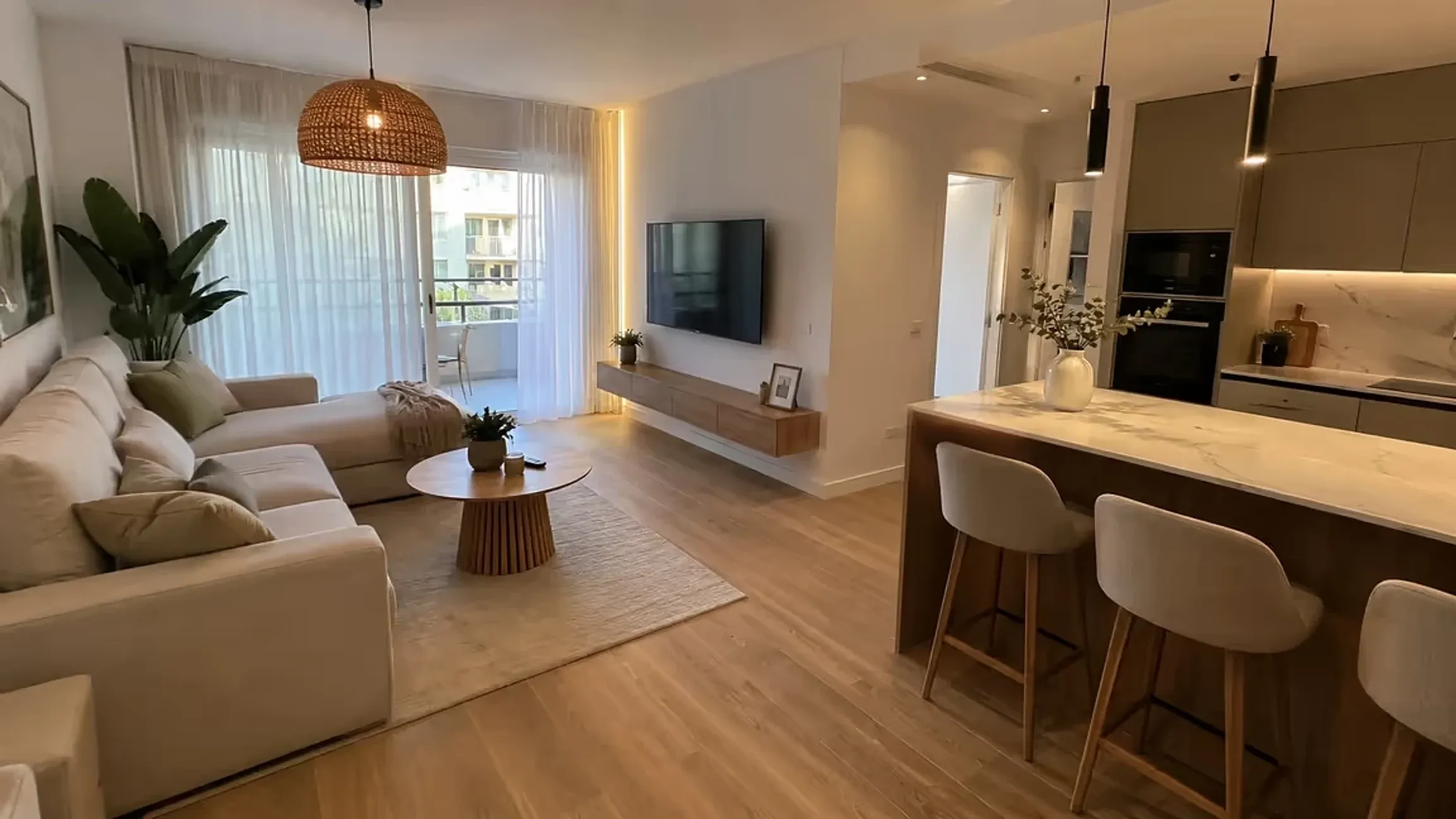 El salón y la cocina abierta de un piso recién reformado: suelo de madera, isla con banquetas y terraza al fondo